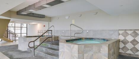 A modern indoor pool area with a central hot tub, a staircase, and a view of the outside.