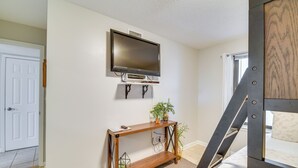A room with a TV mounted on the wall, a wooden console table with a plant, and a bed with a headboard. - Waterfront Pool: Orange Beach Condo w/ Views! (Orange Beach)