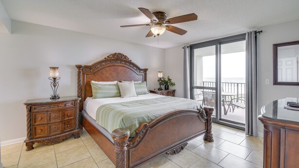 A bedroom with a wooden bed, a ceiling fan, a nightstand, and a view of the outside balcony. - Waterfront Pool: Orange Beach Condo w/ Views! (Orange Beach)