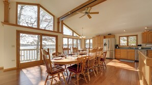 Un vaste espace dédié à la salle à manger, avec une grande table et des chaises en bois, un ventilateur de plafond et de grandes fenêtres offrant une vue sur l’extérieur.