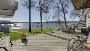 Une terrasse en bois, meublée pour l’extérieur, avec un barbecue et une vue sur un lac où naviguent des bateaux.