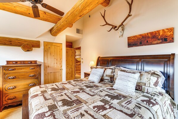 A bedroom with a wooden ceiling, a bed with patterned bedding, a dresser, and a wall-mounted deer antler. - Spacious Rifle Cabin w/ Deck + Mountain Views! (Rifle)