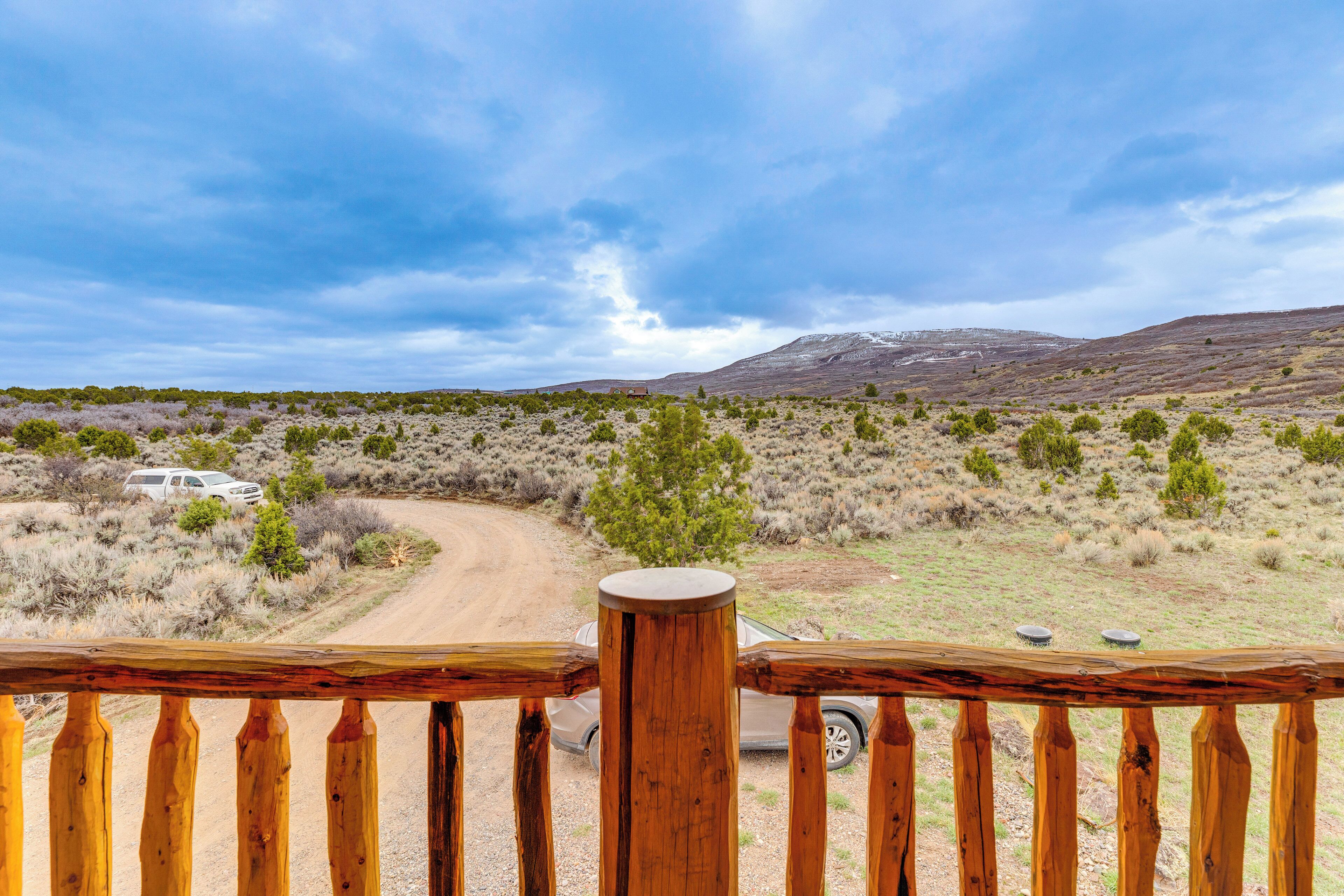 A wooden deck overlooking a dirt road with sparse vegetation and a distant mountain.