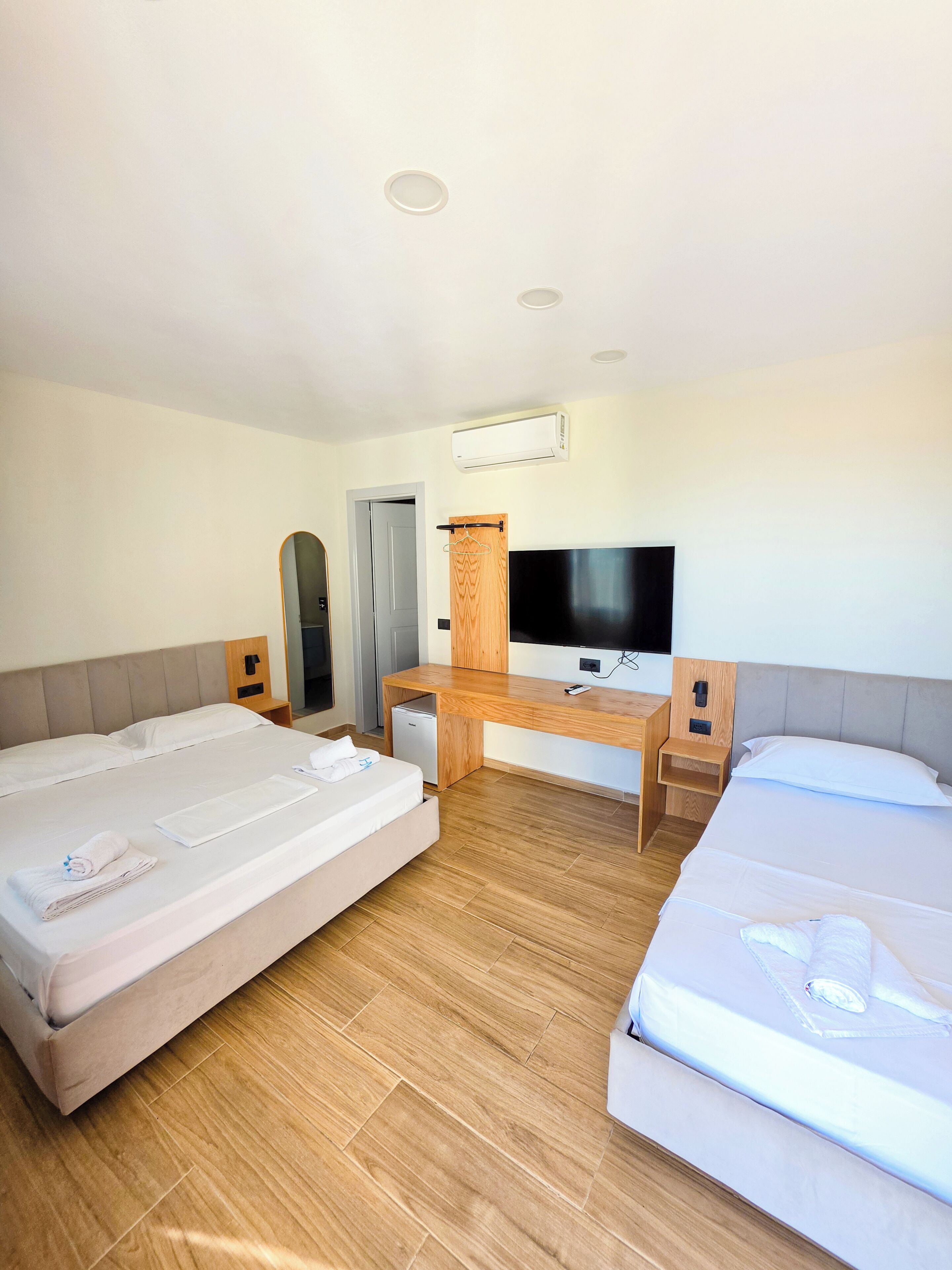 A hotel room with two beds, a desk, a television, and an air conditioning unit.