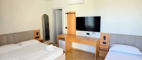 A hotel room with two beds, a desk, a television, and an air conditioning unit.
