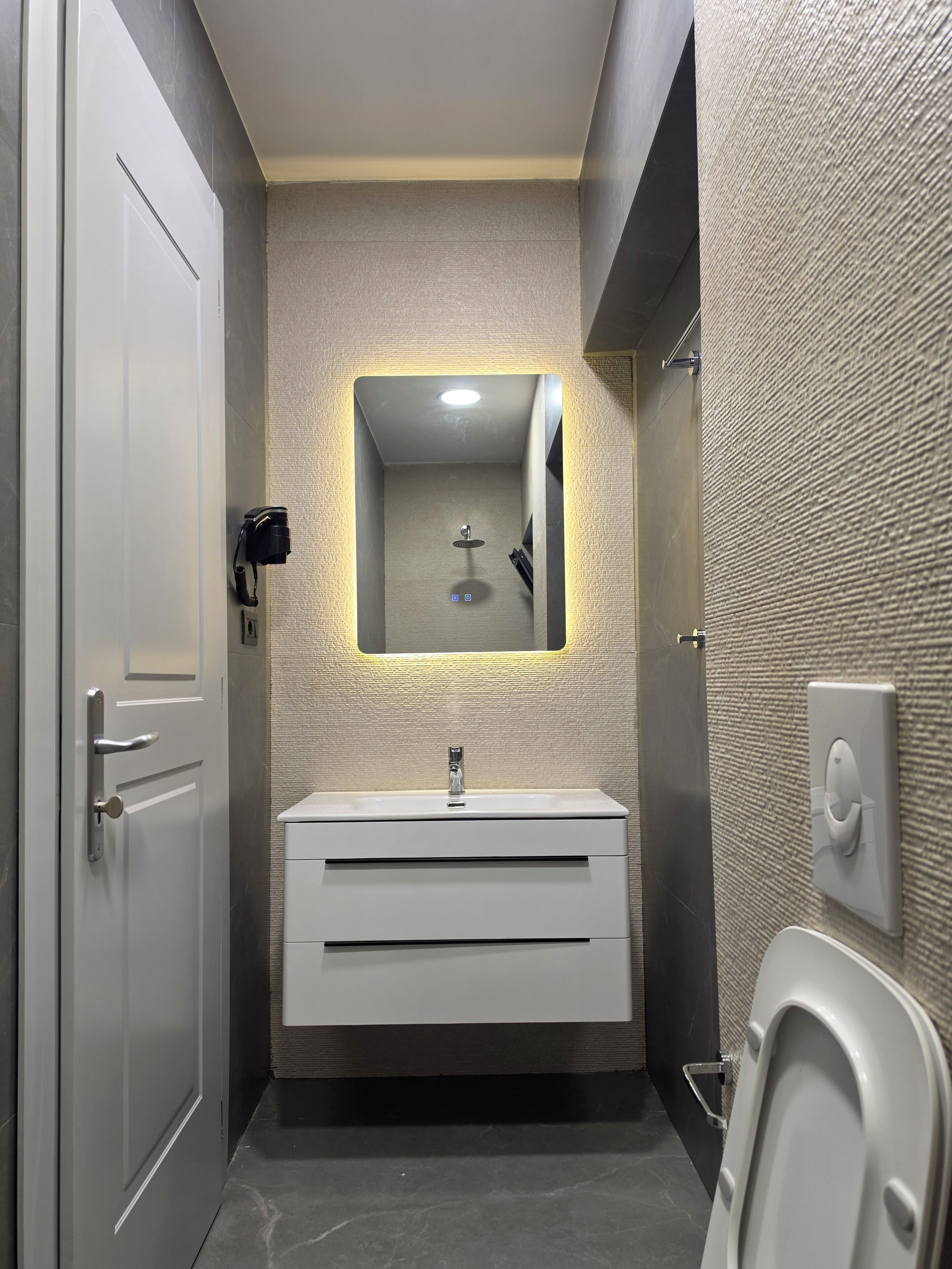 Ein modernes Badezimmer mit einem weißen Waschtisch, einem Spiegel, einer Dusche und einer Toilette.