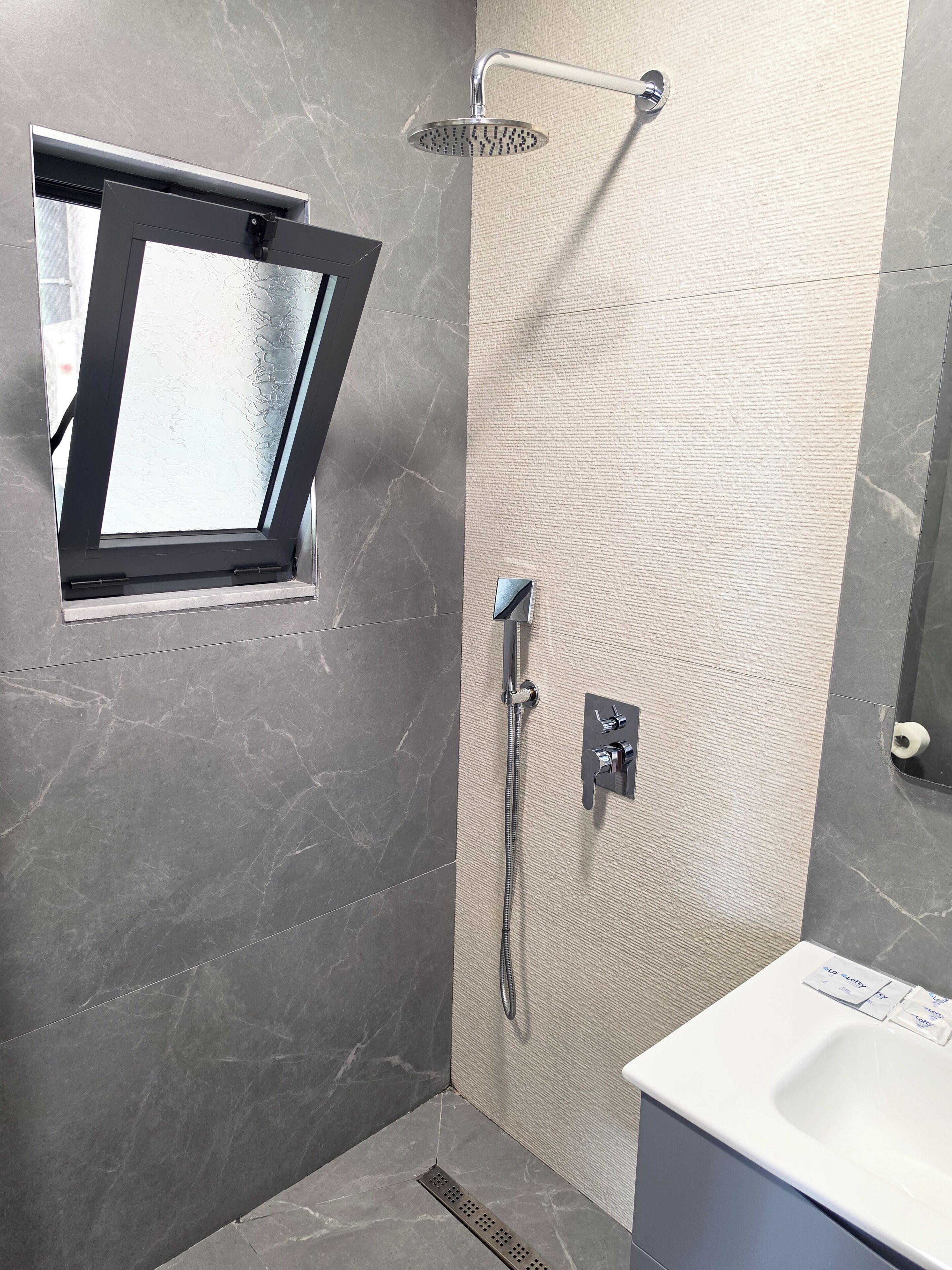 Ein modernes Badezimmer mit Dusche, Fenster und Waschbecken.