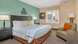 Une chambre d’hôtel comprenant un lit, deux tables de chevet avec des lampes, un canapé, une fenêtre avec des stores et un élément décoratif mural.