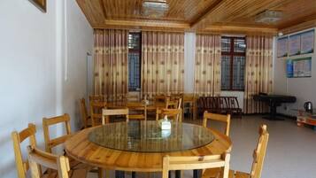 A round table with chairs, a billiards table, and curtains on windows.