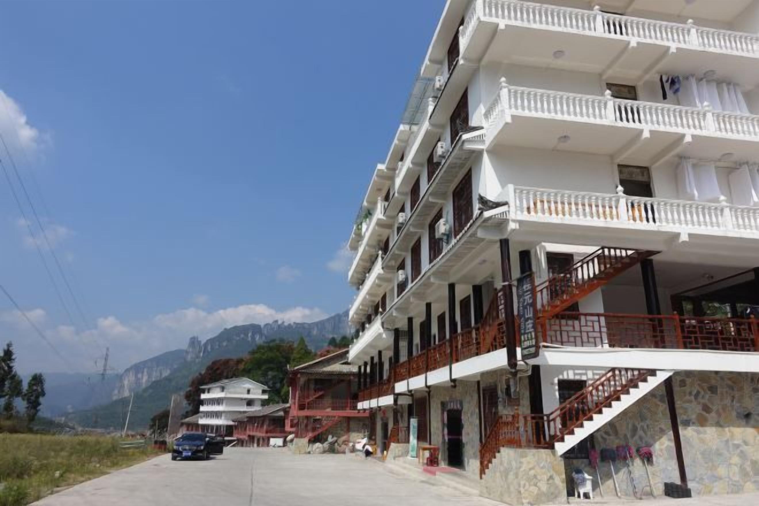 A multi-story hotel with balconies, a staircase, and a view of mountains.