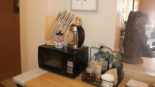 A kitchen counter with a microwave, a coffee maker, and a knife block. There is a framed artwork on the wall and a wooden sculpture in the background.