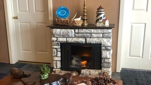 A stone fireplace with a mantelpiece, a small decorative item, and a tray of pinecones and a candle on a wooden table.