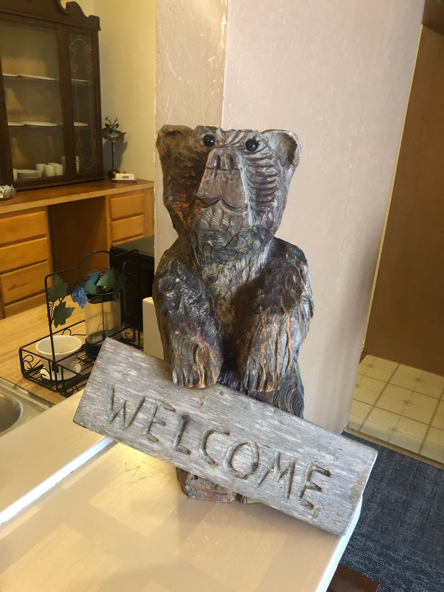 A rustic wooden bear sculpture with a 'WELCOME' sign in front of it.