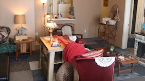 A cozy living room with a wooden table, a red sofa, a lamp, and a small side table with decorative items.