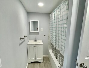 Une petite salle de bain avec un meuble-lavabo blanc, un évier et une douche dotée d’un rideau à pois.