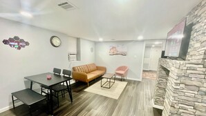 Un salon moderne avec une cheminée en pierre, un coin repas avec une table et des chaises, un canapé et un fauteuil rose.