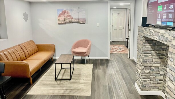 Un salon moderne avec un canapé en cuir, un fauteuil rose, une table basse, une cheminée en pierre et un téléviseur fixé au mur.