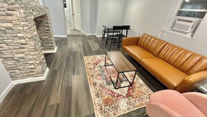 Un salon doté d’une cheminée en pierre, d’un canapé en cuir marron, d’un tapis à motifs et d’un coin repas avec des chaises et une table.