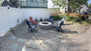 Un patio con baldosas de piedra, un pozo de fuego circular y sillas Adirondack.
