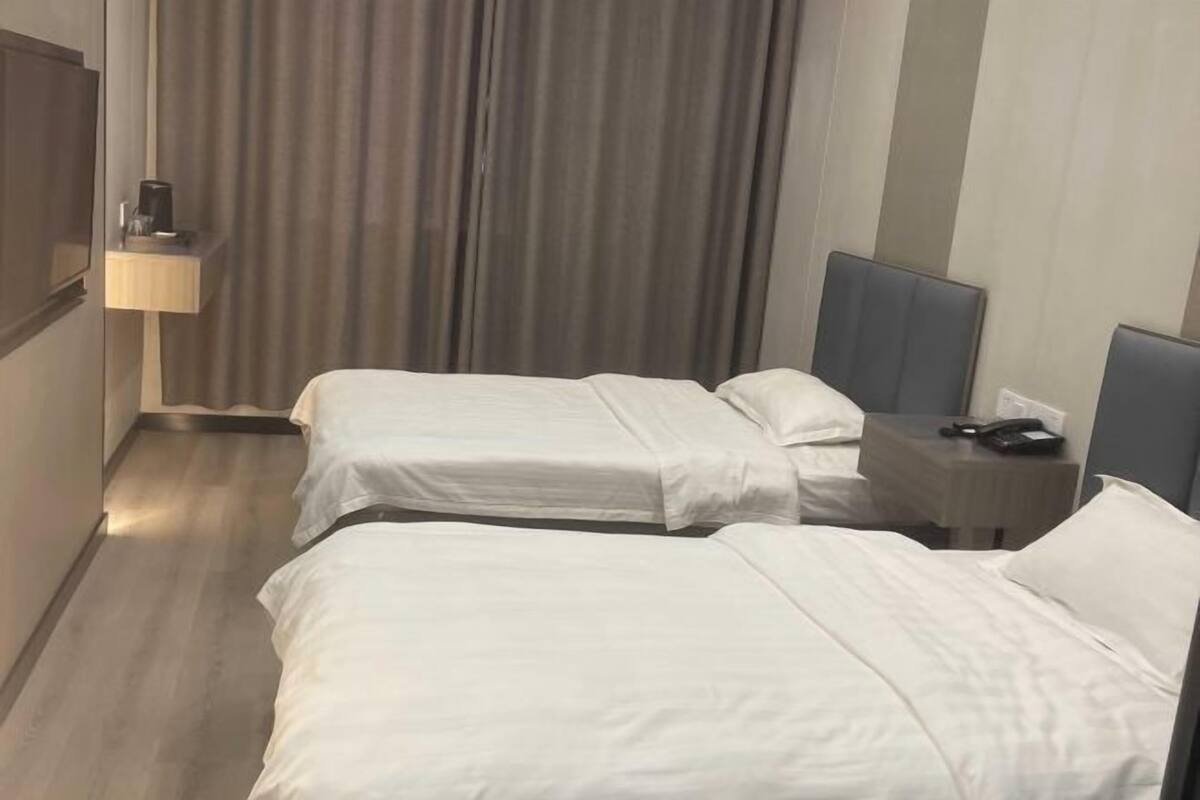 Una habitación de hotel con dos camas, una mesita de noche con lámpara y una cortina.