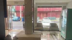 A hotel lobby with a glass door leading outside, a seating area with chairs, a vending machine, and a small table with a decorative item. - Huainan Longmen Hotel (Huainan)