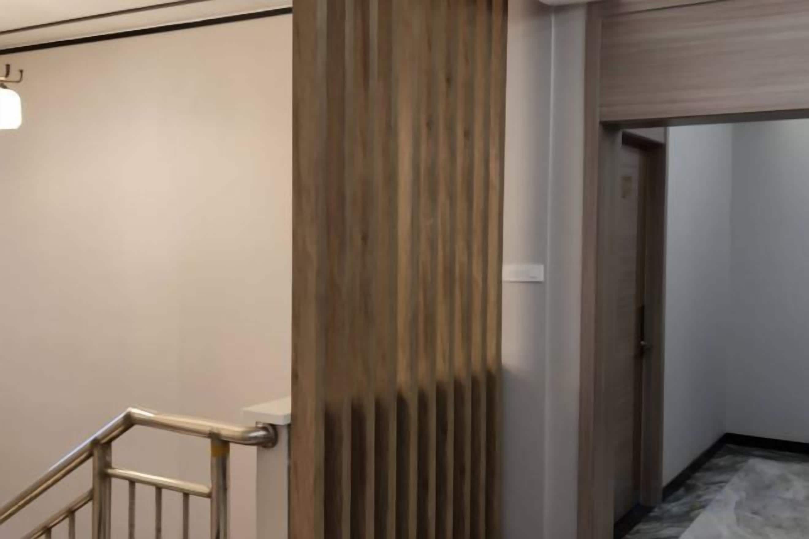 A hallway with a wooden panel wall, a metal railing, and a door leading to another room.