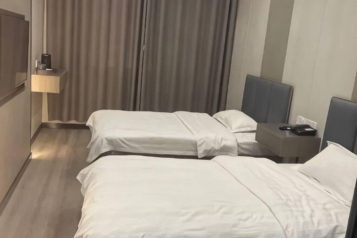 Habitación de hotel con dos camas, una mesita de noche, una lámpara y una cortina.