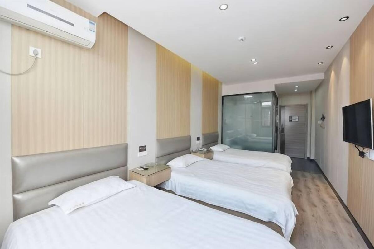 Habitación de hotel con dos camas, un televisor y un vidrio corredizo que da a un pasillo.