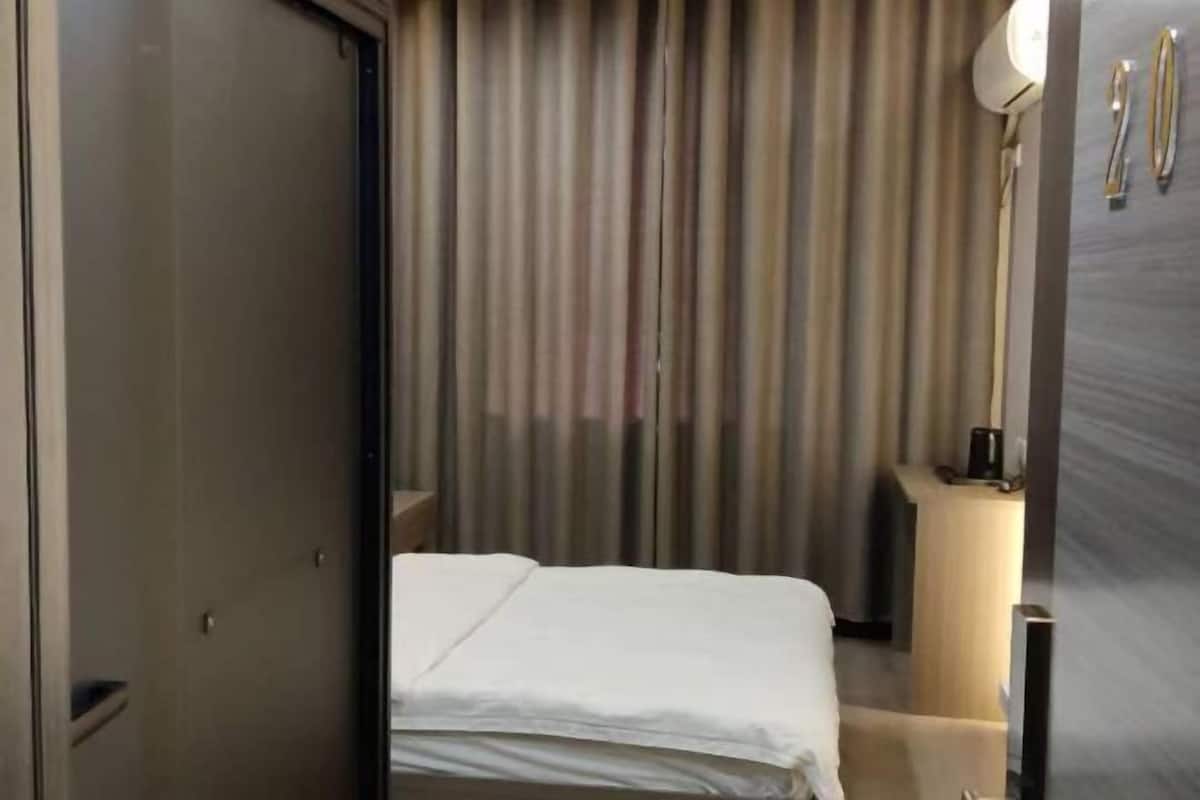 Una habitación de hotel con cama, cortinas, una mesita de noche y una lámpara.