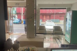 Vestíbulo de hotel con puerta de vidrio que da al exterior, una máquina expendedora y una zona de estar con sillas.