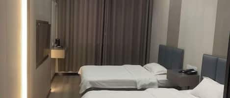 A hotel room with two beds, a bedside table with a lamp, a nightstand, and a curtain.