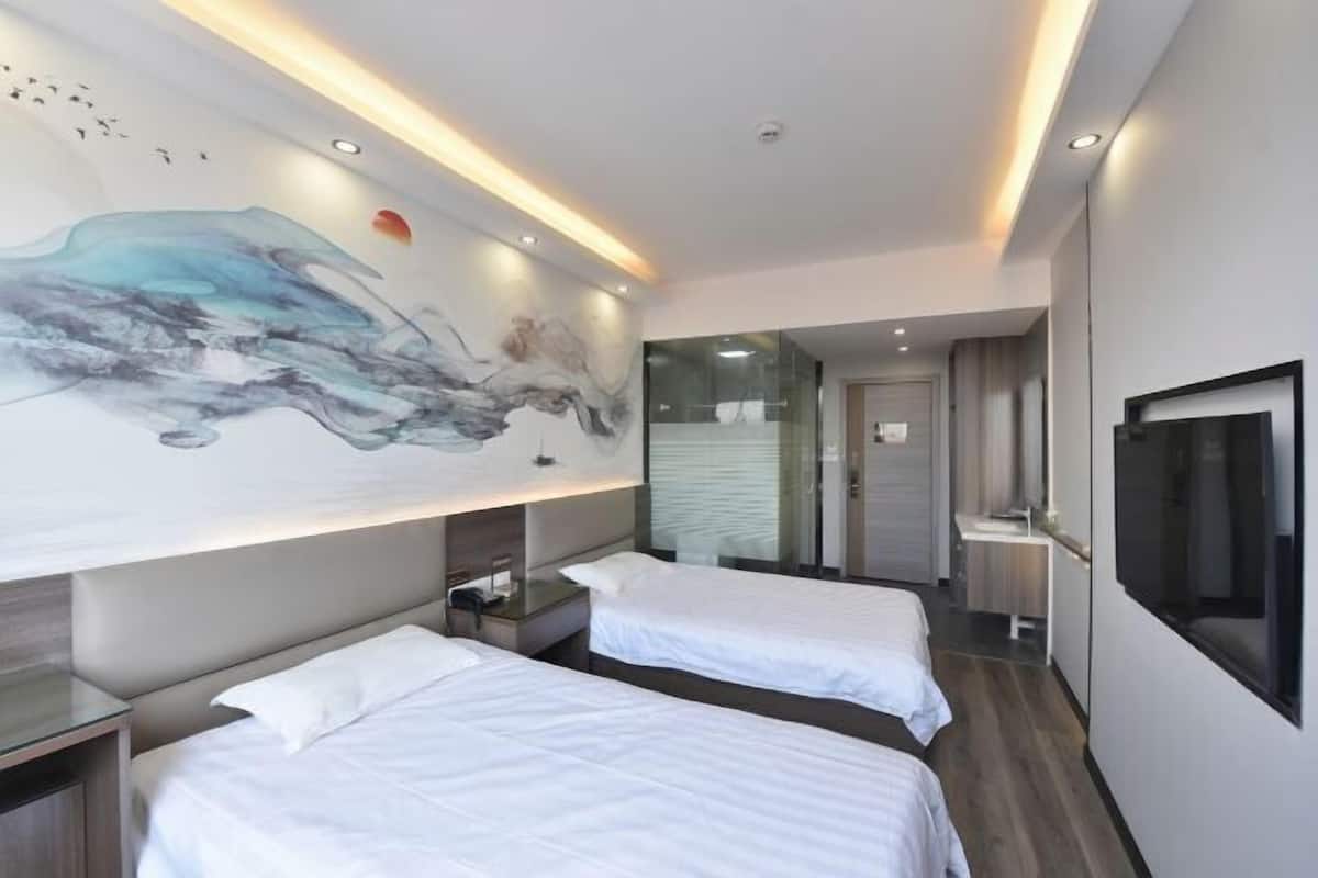 Habitación de hotel con dos camas, un amplio mural abstracto en la pared, televisión y baño moderno con ducha de vidrio.