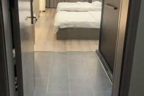 Ein schmaler Flur führt zu einem Bett mit einem hölzernen Kopfteil und weißer Bettwäsche.