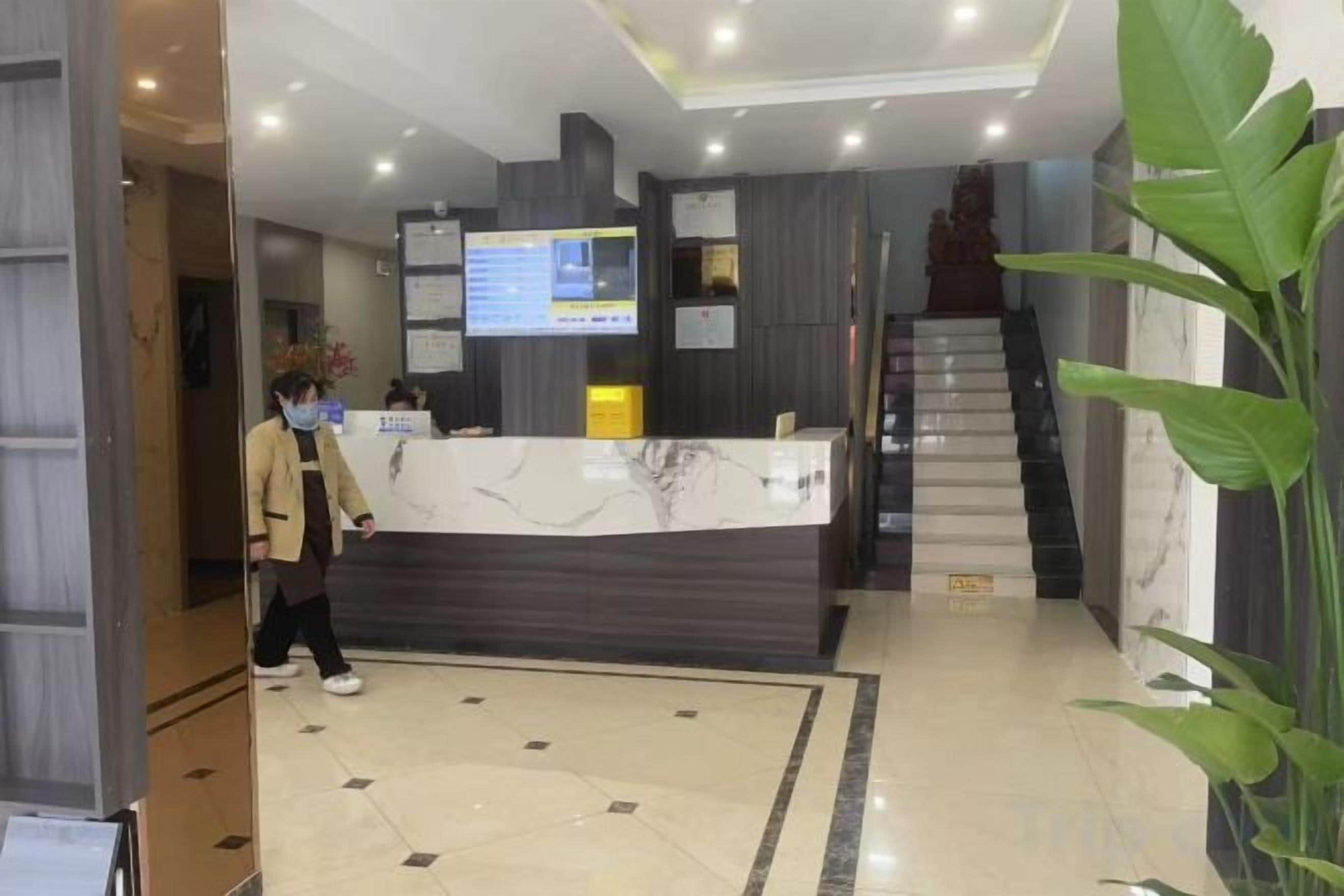 Zona de recepción de hotel con mostrador de mármol, pantalla digital y una escalera.