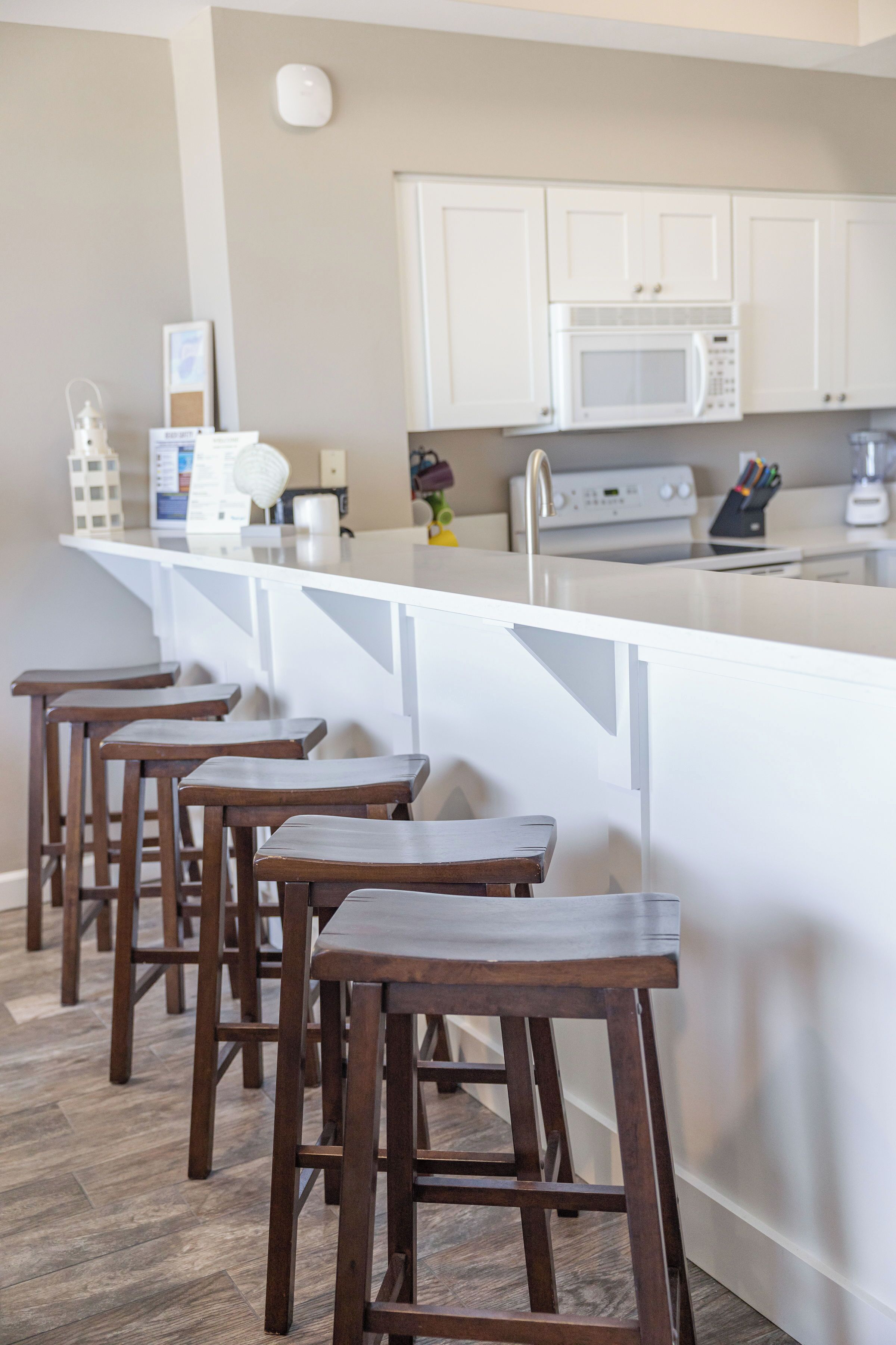 A kitchen with white cabinets, a microwave, and wooden stools.