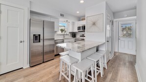 A modern kitchen with white cabinetry, stainless steel appliances, and a central island with bar stools. - Steps to the beach and Dock on the Bay! Pool, family and pet friendly! (Gulf Shores)