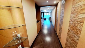 A narrow hallway with wooden flooring, a glass display unit, and a stone-textured wall. - 5C - 2 Bedroom Downtown Apartment With Shared Pool (Bangkok)