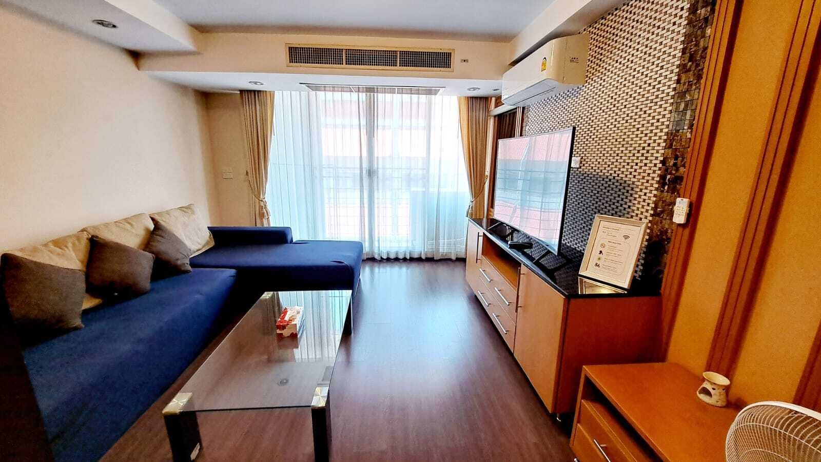 A compact living space with a sofa, a small table, a kitchenette, and a large window with curtains.