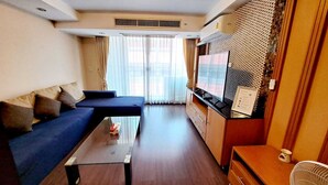 A compact living space with a sofa, a small table, a kitchenette, and a large window with curtains. - 5C - 2 Bedroom Downtown Apartment With Shared Pool (Bangkok)