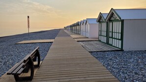 Ein hölzerner Steg führt zu Strandhäusern, am Anfang befindet sich eine Bank.
