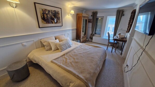 A hotel room with a large bed, a desk, a chair, a lamp, and a painting on the wall.