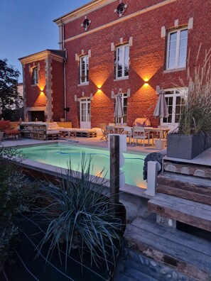 A brick building with a pool, outdoor seating, and a well-lit facade.