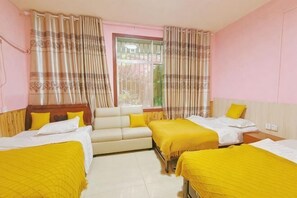 Quarto de hotel com três camas, um sofá e uma janela com cortinas.
