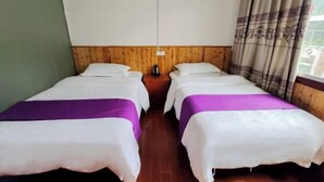 Ein Zimmer mit zwei Betten, jeweils mit weißer und violetter Bettdecke, einem Holz-Kopfteil und einem Nachttisch mit Wasserkocher.