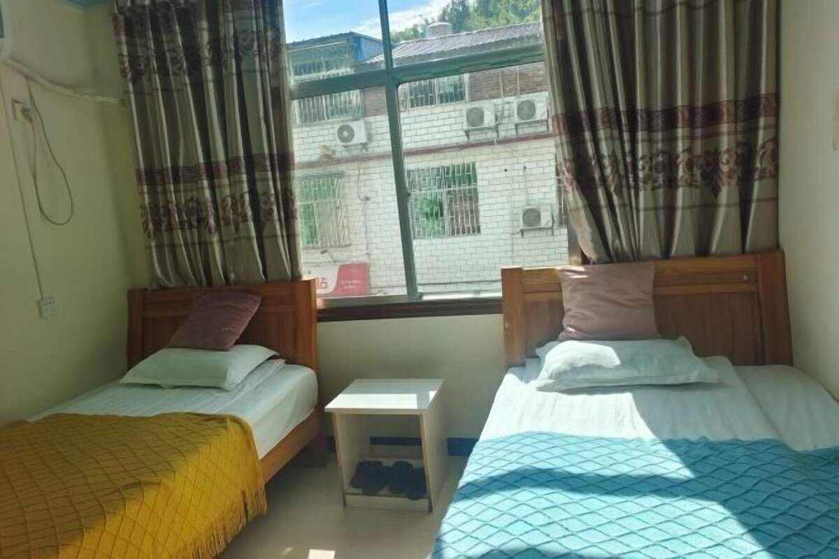 Une chambre avec deux lits, une petite table de chevet blanche et une fenêtre avec des rideaux.