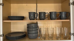 Ein Schrank mit Regalen, der schwarzes Geschirr, graue Tassen und klare Gläser beherbergt.
