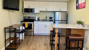 Eine kompakte Küche mit weißen Schränken, einem Edelstahl-Kühlschrank, einer Mikrowelle, einem Backofen und einem Holztisch mit Hocker.