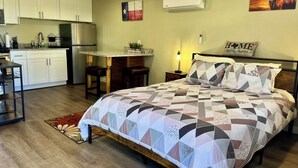 Ein Schlafzimmer mit Bett, Nachttisch, Schreibtisch und einer Küchenzeile.