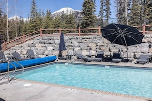 Un espace piscine avec des chaises longues, une plateforme flottante bleue et un mur en pierre en arrière-plan.