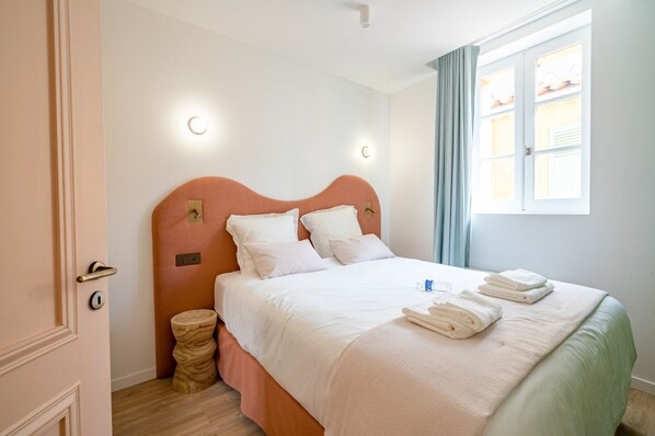 A neatly made bed with white linens and towels, a wooden headboard, and a window with curtains. - Résidence Saint-Tropez FENIERS (Saint-Tropez)